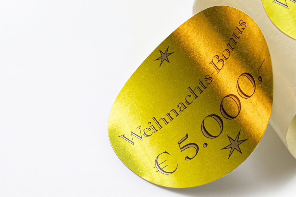 Złota owalna etykieta lakierowana z napisem Weihnachts-Bonus i gwiazdkami na rolce